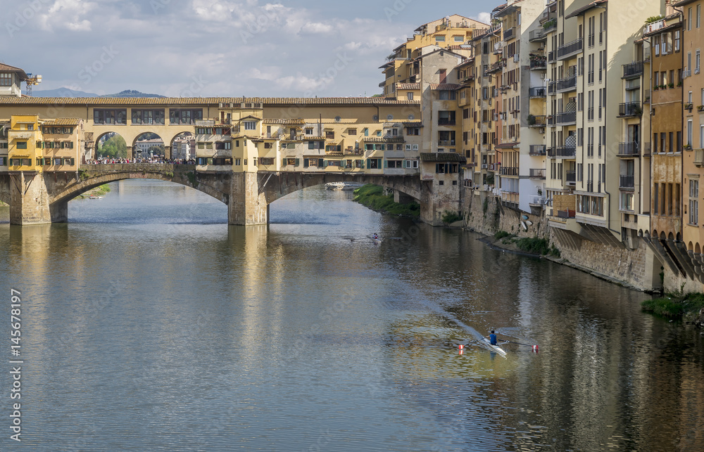 Rowing boats navigate the Arno river near the famous Ponte Vecchio bridge, historic center of Florence, Italy