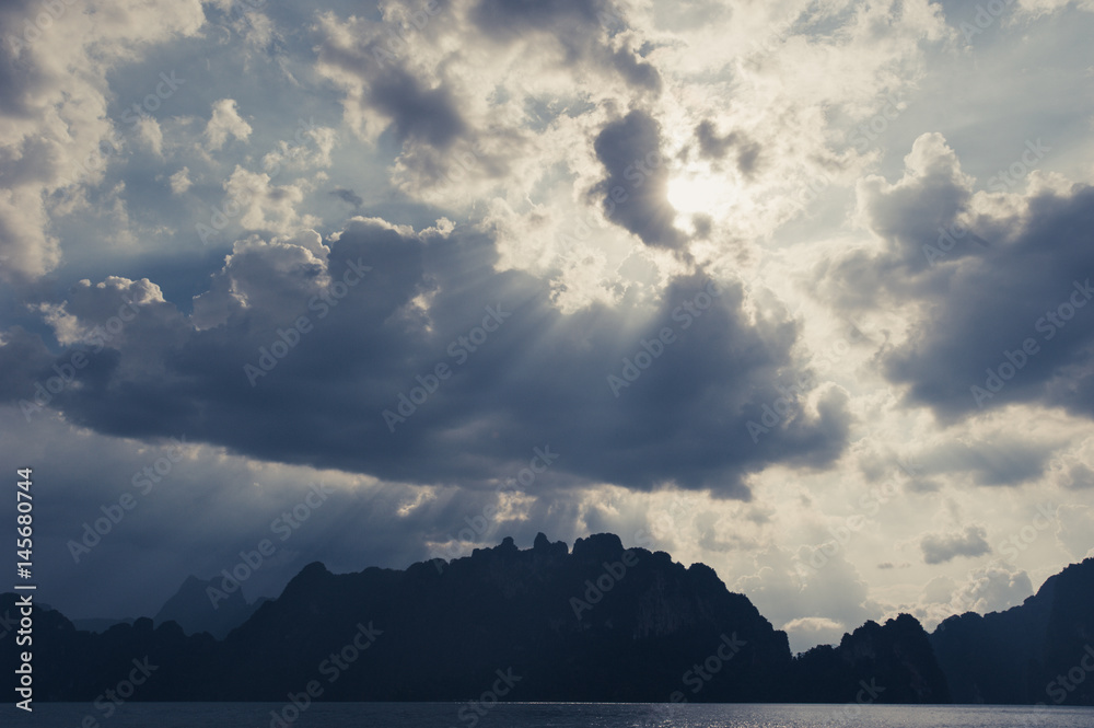 Beautiful sun rays through the clouds over mountains,evening light,Amazing scene at Khao-Sok National Park of Thailand Beautiful sun rays through the clouds over mountains,evening light,Amazing scene at Khao-Sok National Park of Thailand