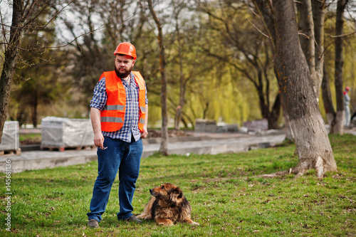 Portrait of brutal beard worker man suit construction worker in safety orange helmet with watchdog.