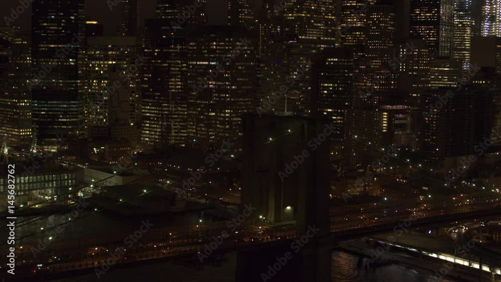 AERIAL HELI SHOT, CLOSE UP: Flying above busy jammed interstate on iconic Brooklyn Bridge lit up with lights leading to Downtown Manhattan business district. Commuters traveling from work after sunset AERIAL HELI SHOT, CLOSE UP: Flying above busy jammed interstate on iconic Brooklyn Bridge lit up with lights leading to Downtown Manhattan business district. Commuters traveling from work after sunset