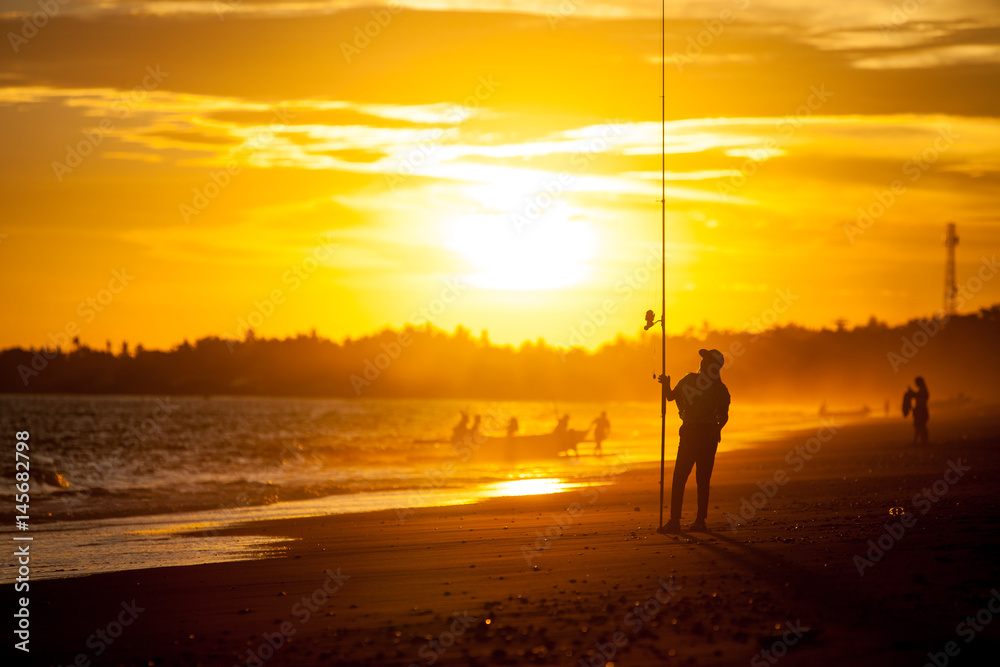 Silhouette of a girl on the beach with a fishing rod in the summer