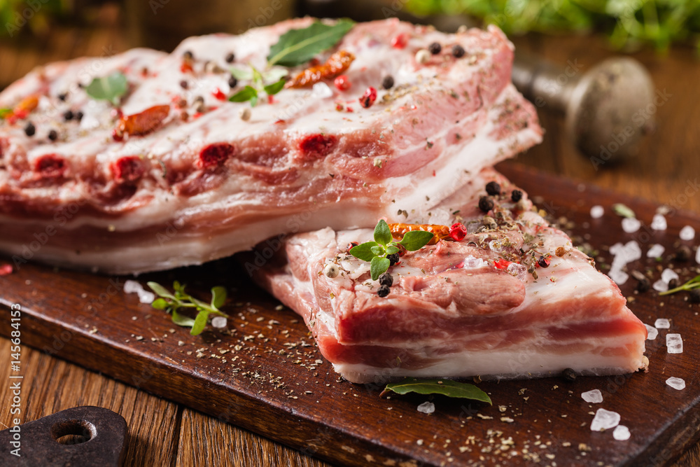 Raw pork ribs, on a plate sprinkled with spices.