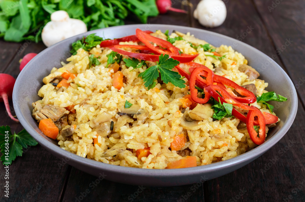 A traditional Asian dish - pilaf with meat, mushrooms and pepper capi in a bowl on a dark wooden background. A traditional Asian dish - pilaf with meat, mushrooms and pepper capi in a bowl on a dark wooden background.