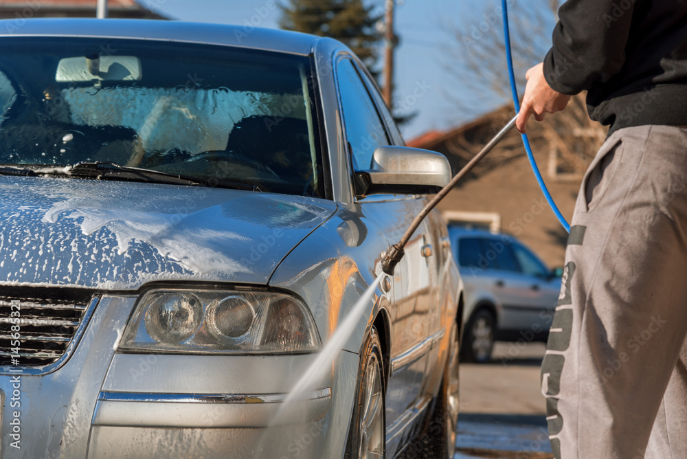 Fototapeta premium Worker in auto service is washing a luxury car by water hoses, backlight