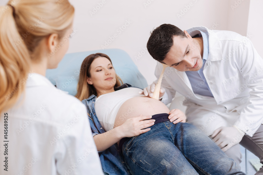 Concentrated obstetricians providing pregnant abdomen checkup in the clinic Concentrated obstetricians providing pregnant abdomen checkup in the clinic
