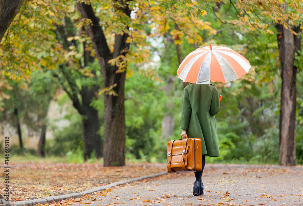 photo of beautiful young woman with umbrella and suitcase on the wonderful autumn park background