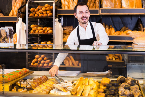 Male shop assistant demonstrating fresh delicious pastry in bakery
