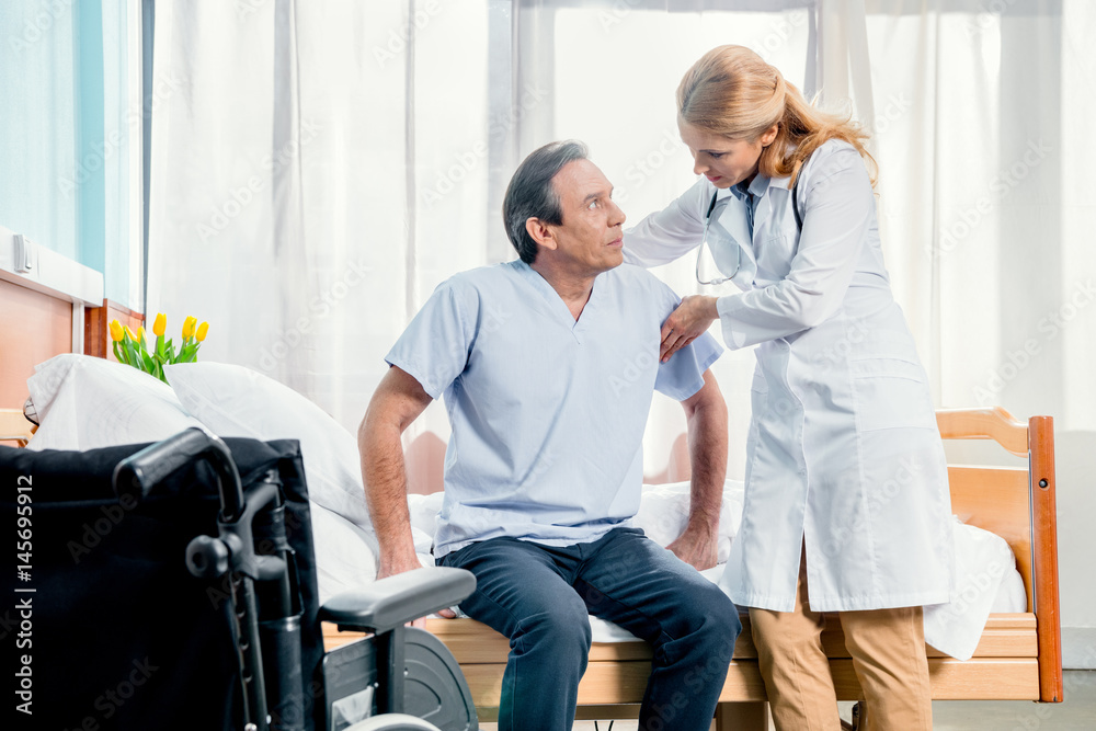 middle aged patient sitting on bed and doctor standing near him in hospital middle aged patient sitting on bed and doctor standing near him in hospital