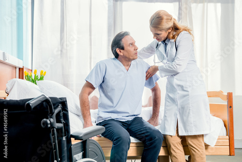 middle aged patient sitting on bed and doctor standing near him in hospital