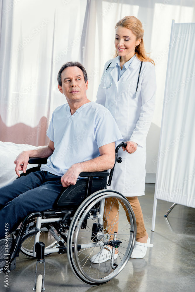 elderly man sitting in wheelchair and doctor standing near him in hospital