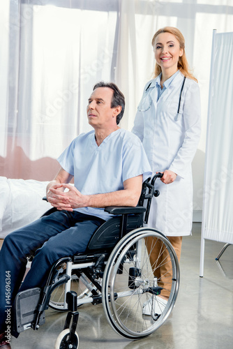 elderly man sitting in wheelchair and doctor standing near him in hospital