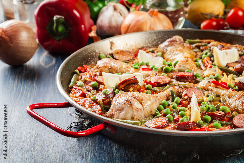 Traditional paella with chicken legs, sausage chorizo and vegetables served in paellera Traditional paella with chicken legs, sausage chorizo and vegetables served in paellera