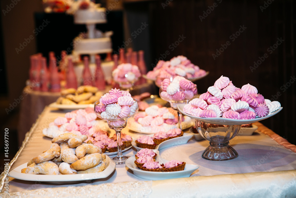 Sweet multilevel white wedding cake decorated with pink bottles of champagne. Candy bar