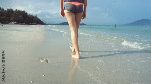 Woman walking on beach barefoot at sunset. Female strolling on sand near sea.