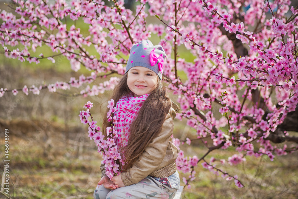 Cute beautiful stylish dressed blond girl standing on a field of spring young peach tree with pink flowers.smiling girl dressed in in pink in spring season. Cute beautiful stylish dressed blond girl standing on a field of spring young peach tree with pink flowers.smiling girl dressed in in pink in spring season.