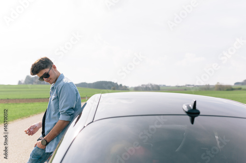 Young man leaning on car waiting