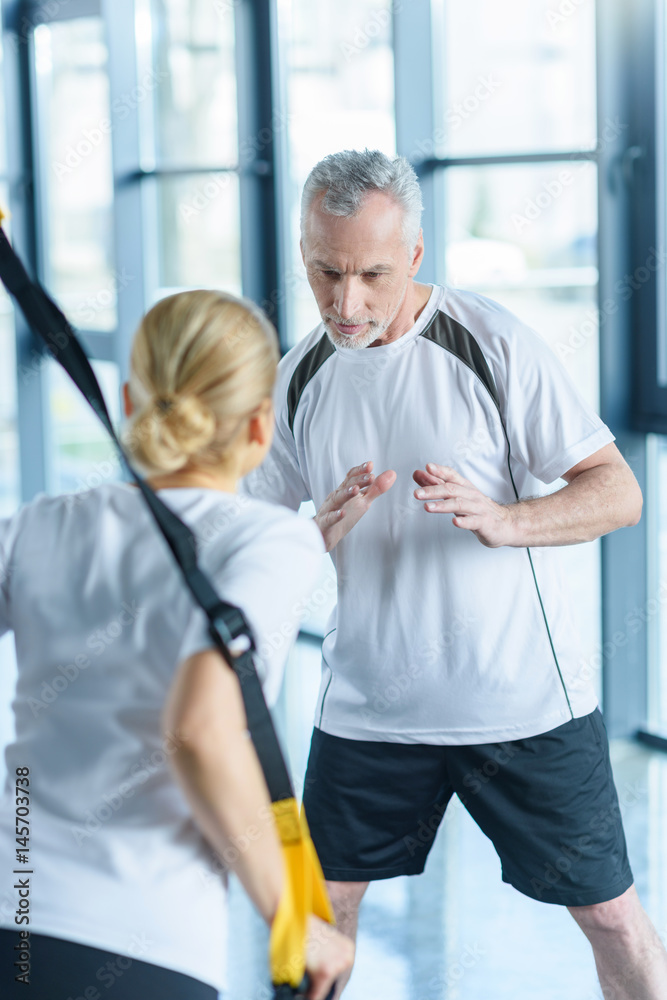 sportswoman and senior trainer training with resistance band in sports center