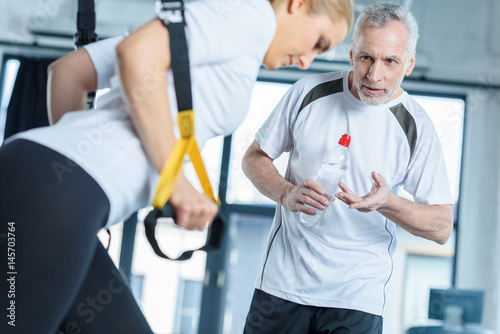 sportswoman and senior trainer training with resistance band in sports center