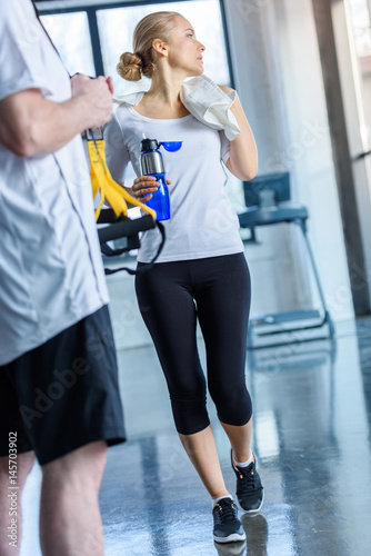 sportswoman with towel holding sport bottle in sports center