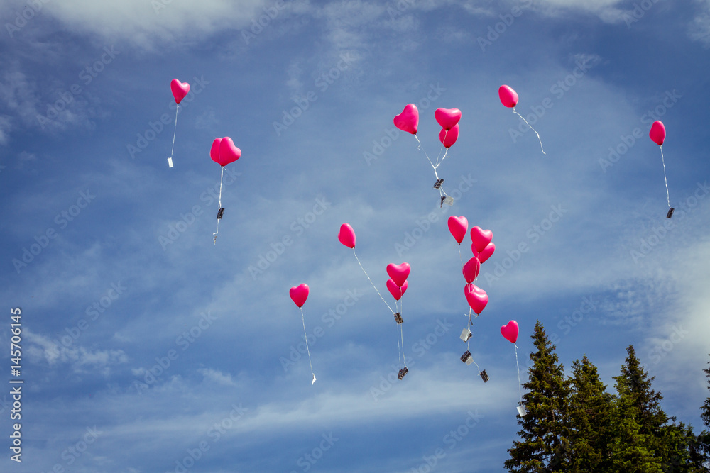 pink heart balloons flying in blue sky at wedding