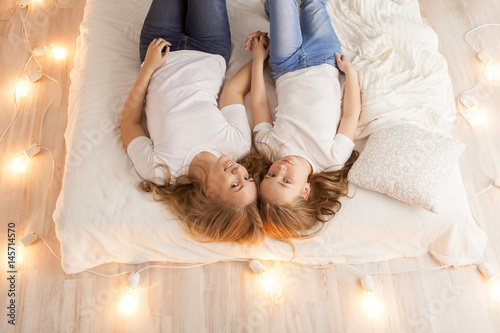 Mother and daughter lay on the bed and look at the camera. View from above. Togetherness. Loft interior