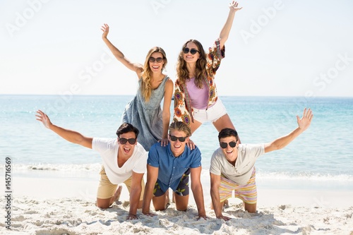 Friends forming pyramid with arms raised at beach