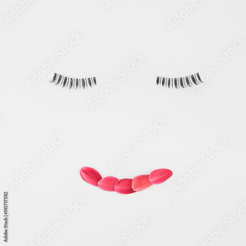 Fake eyelashes and red petals lip on white background