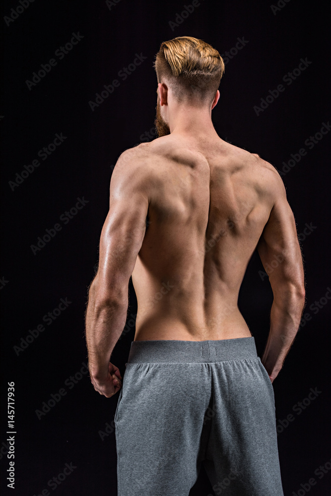 back view of shirtless bearded bodybuilder posing isolated on black in studio