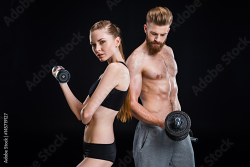 sportswoman and sportsman training with dumbbells isolated on black in studio