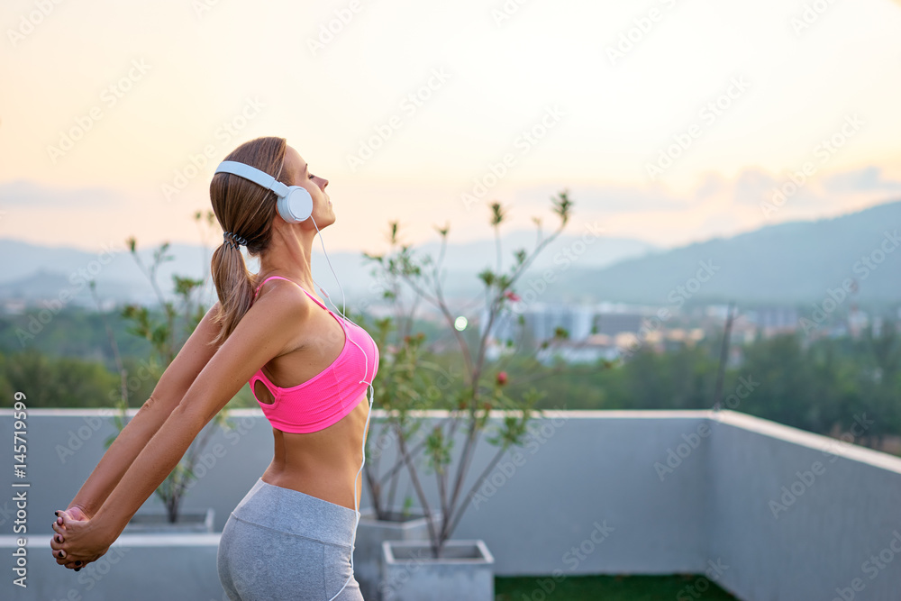 Music and fitness. Young woman in sports wear with headphones stretching outdoors.