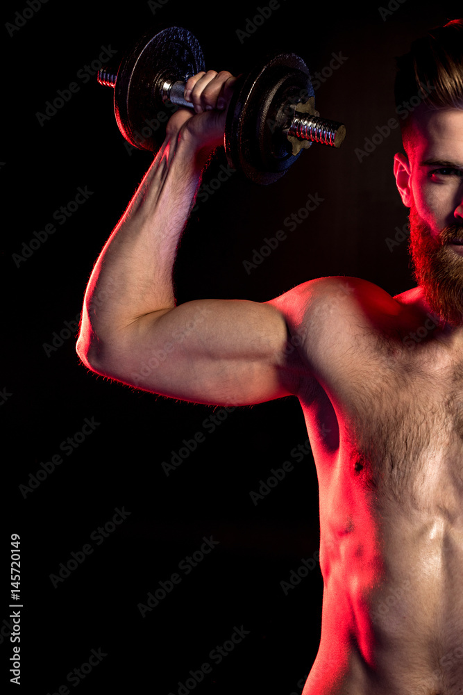 handsome bodybuilder training with dumbbell isolated on black with dramatic lighting handsome bodybuilder training with dumbbell isolated on black with dramatic lighting
