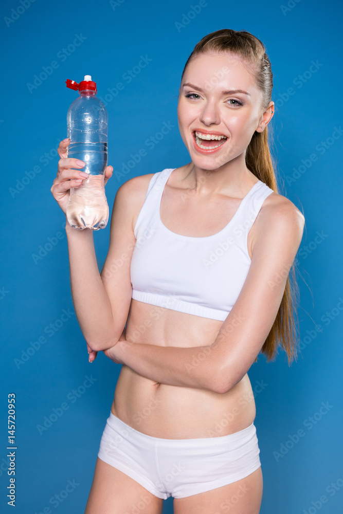 young sportswoman holding sport bottle with water isolated on blue young sportswoman holding sport bottle with water isolated on blue