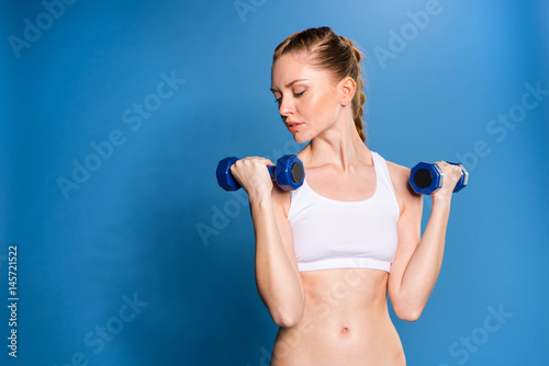 young sportswoman training with dumbbells isolated on blue in studio © LIGHTFIELD STUDIOS