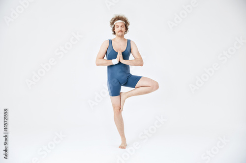 Man in old style sport clothing practicing yoga. Vrikshasana with eyes closed