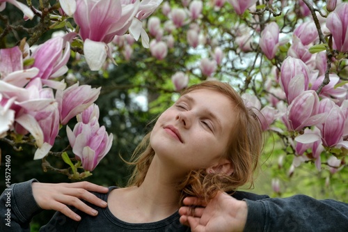 Mädchen mit geschlossenen Augen  unter Magnolienblüten   ( Magnoliaceae ) , Hände an den Schultern
