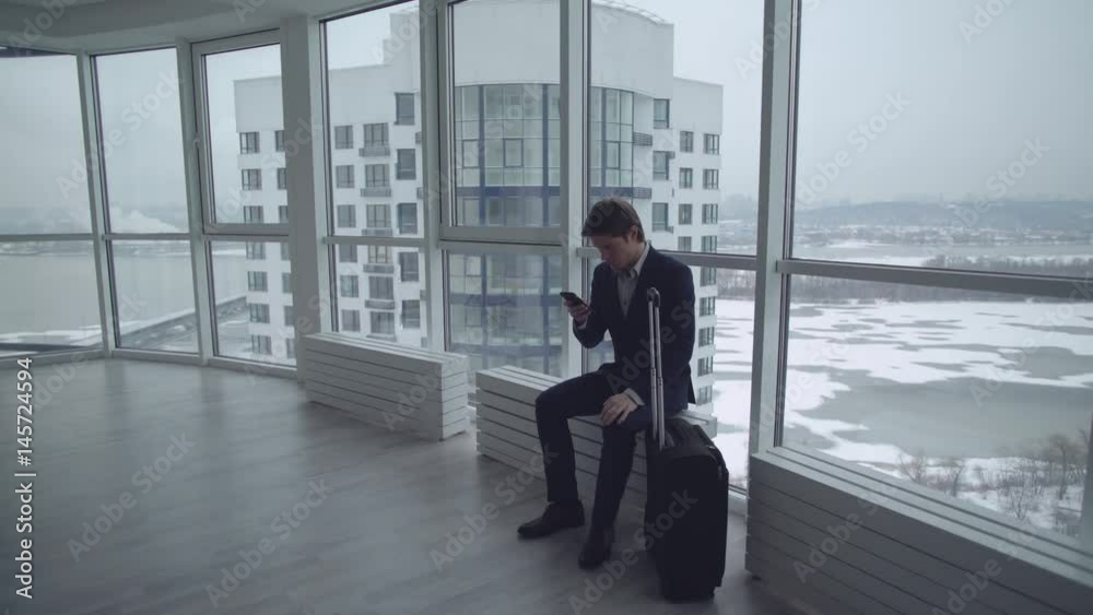 young man with suitcase using app on smartphone. Businessman waiting play game. young man with suitcase using app on smartphone. Businessman waiting play game.