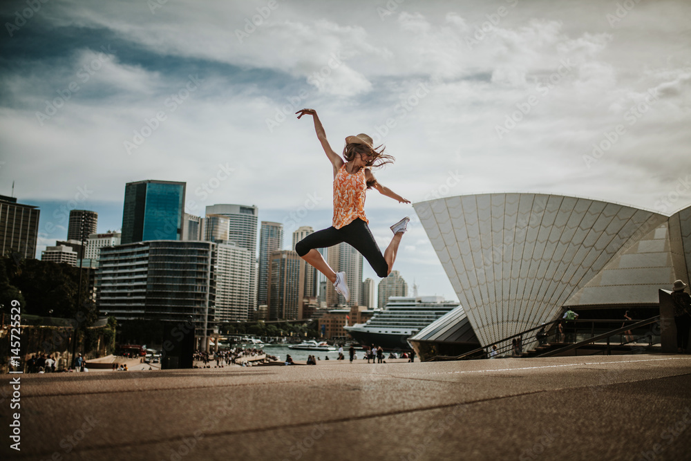 Naklejka premium Szczęśliwa kobieta skacząca w powietrzu w Sydney, z panoramą miasta w tle. Australia.