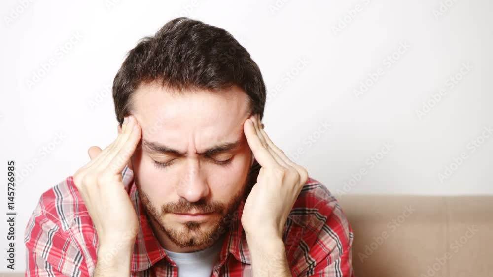 Headache, Tired, Stressed concept. Closeup of young man sitting on sofa suffering from headache Headache, Tired, Stressed concept. Closeup of young man sitting on sofa suffering from headache