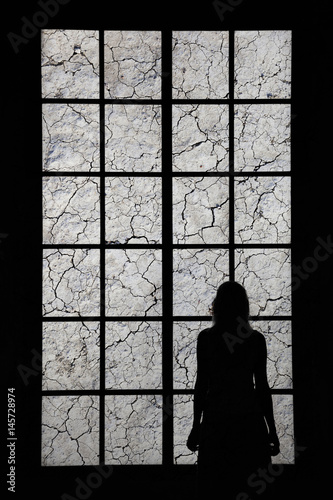 Lonely woman looking through big cracked window and thinking about things. Conceptual lonely or sad women silhouette background.