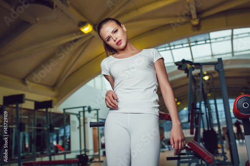 Beautiful girl standing in the gym dressed blank white t-shirt and tights. Mock up.