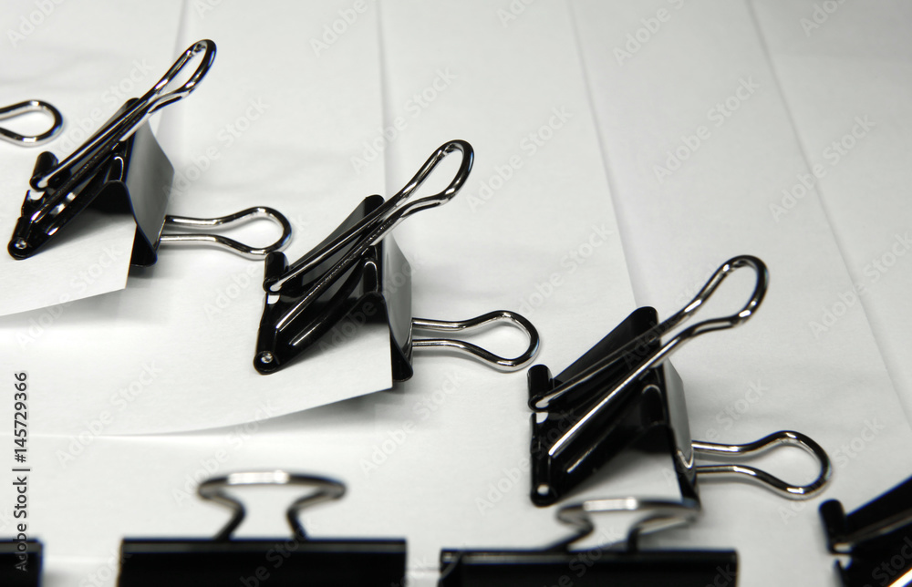 Black binder clips in a row clamping the paper close up white background Black binder clips in a row clamping the paper close up white background
