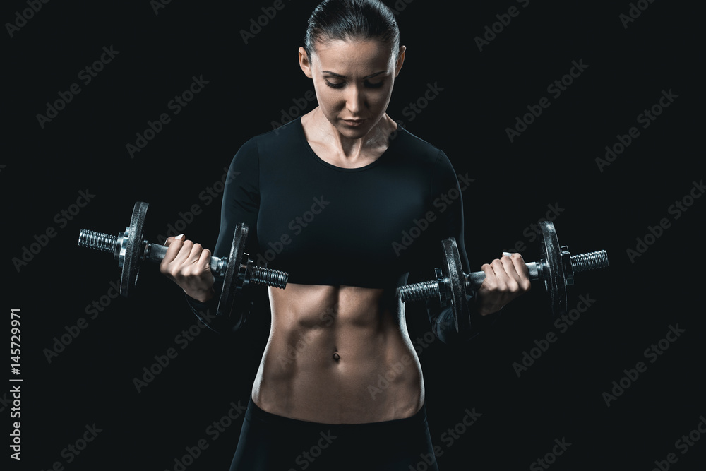 young fitness woman training with dumbbells isolated on black.