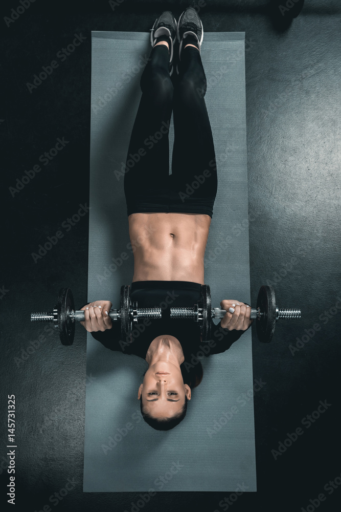 young fitness woman training with dumbbells and lying on mat