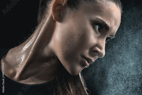 Fotografie Close-up portrait of young sweaty fitness woman looking away on black