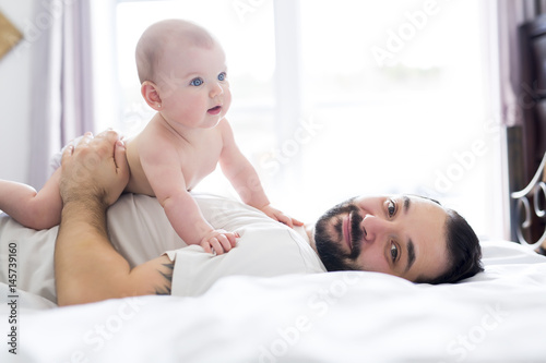 Young happy father playing with babyon bed photo