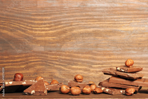 wooden background with a tower of slices of milk chocolate and hazelnuts. copy space.