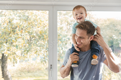 Toddler boy on father's shoulders at home by window
