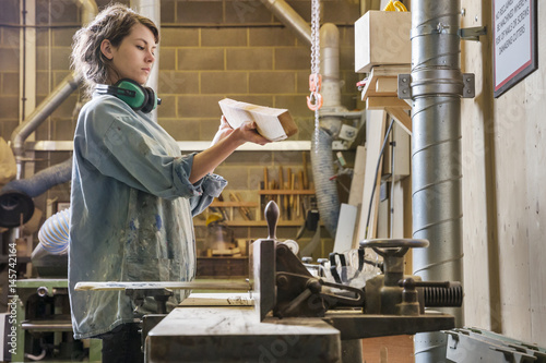 Young woman examining wood after cutting on machine in a workshop