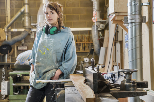 Portrait of young woman next to machinery in wood workshop