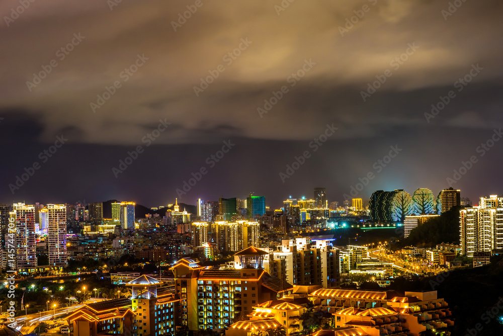 Fototapeta premium Night cityscape with clouds illuminated with city lights. Sanya town, Hainan Island of China.